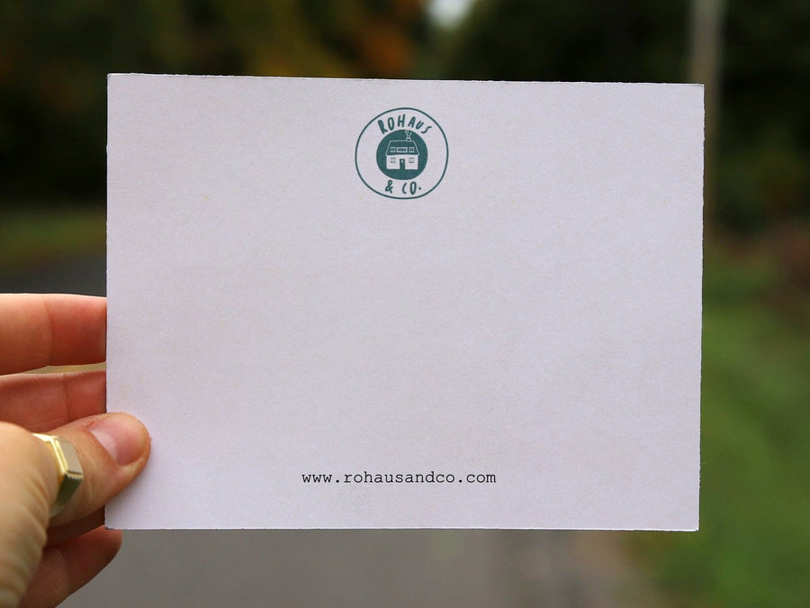A RoHaus & Co. notecard held up on a tree-lined road