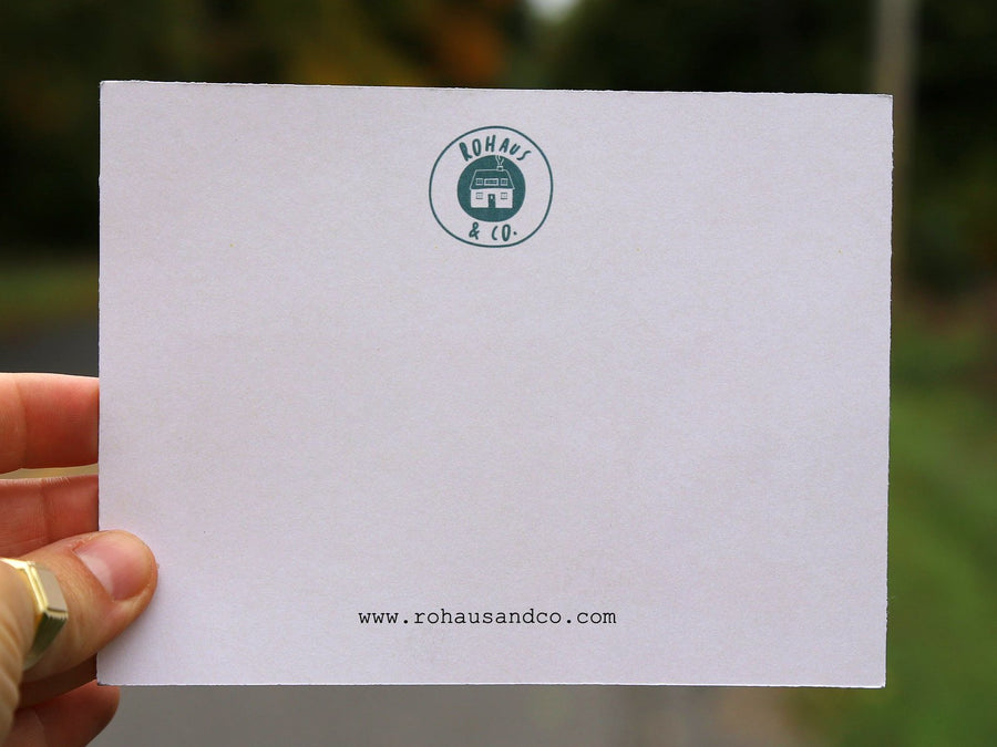 A RoHaus & Co. notecard held up on a tree-lined road, wide view