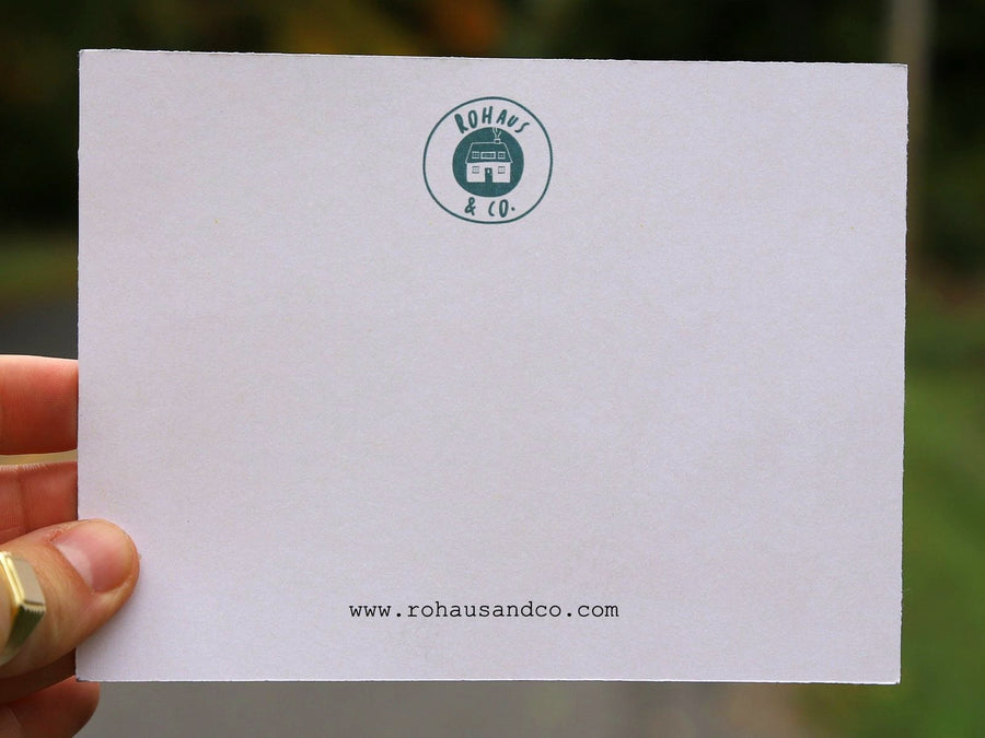 A RoHaus & Co. notecard held up close on a tree-lined road