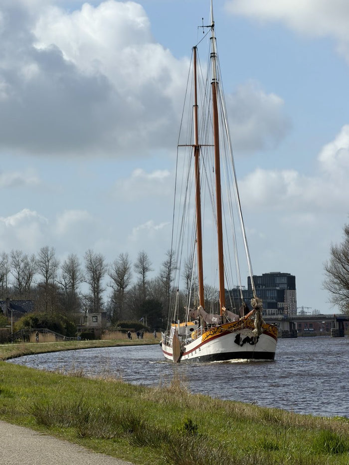 A tall sailing ship on a canal under a cloudy sky