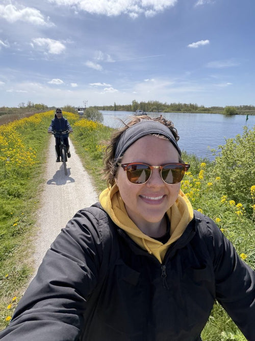 Alex on a path by the water, smiling in sunglasses